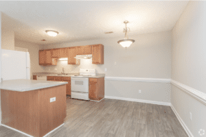 A galley-style kitchen with wood cabinets and white appliances with room for a dining area on the right