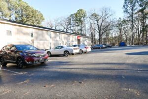 A long, beige apartment building with a large parking lot in the Magnolia Crossing apartment community