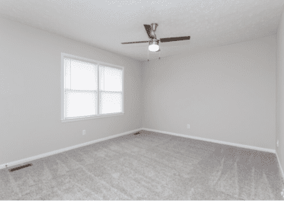 An empty bedroom with light carpet and a ceiling fan