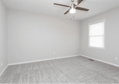 An empty bedroom with light carpet and a ceiling fan