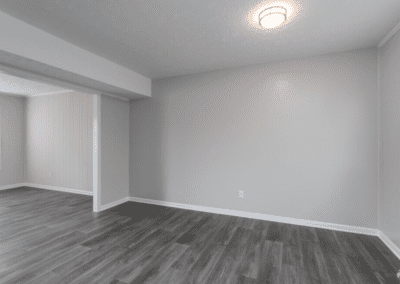 An empty dining room with grey wood floors and an arch that opens to the living room