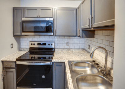 A kitchen with grey cabinets, a white tile backsplash, and stainless steel appliances