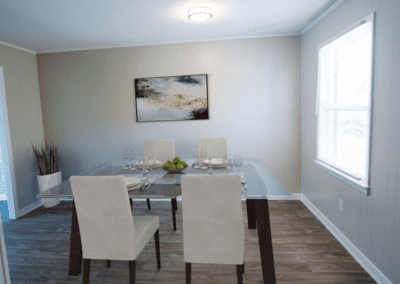 A dining room staged with a glass-top table and four creme upholstered chairs