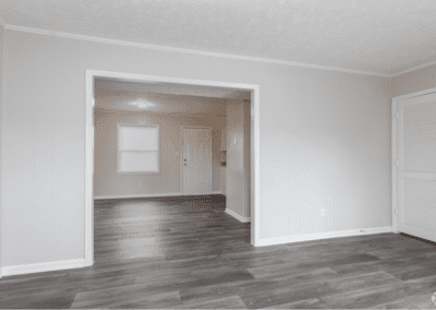 An empty living room with an archway leading to the dining room and kitchen