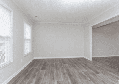 An empty living room with grey wood floors and an arch the opens to the dining room