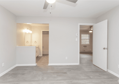 An empty bedroom with a view of the bathroom sink and bathroom beyond, and a door to the living room