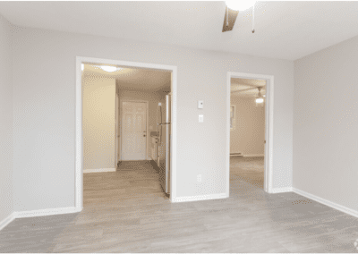 An empty living room with a view of the kitchen through an archway and a door to the bedroom