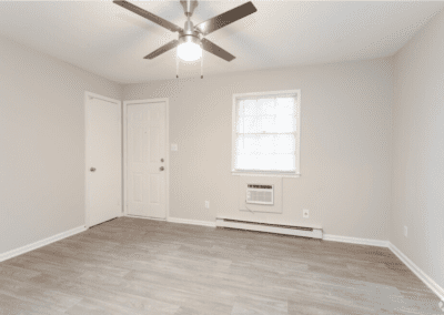 An empty living room with light wood floors and a ceiling fan