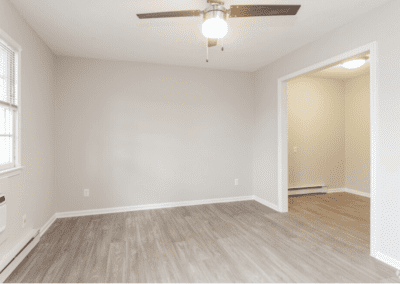 An empty living room with light wood floors and a ceiling fan