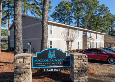 A two-story apartment building with a sign in front declaring it the Magnolia Crossings Apartments