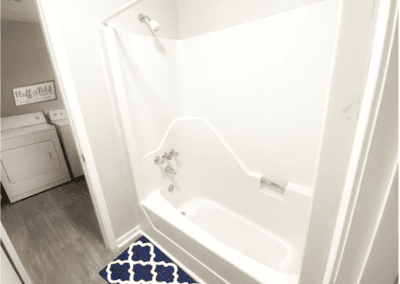 A white bathtub/shower combo with a view of a washer and dryer in the next room