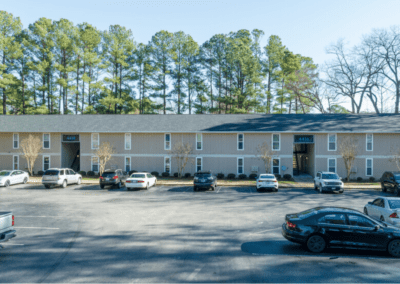 One of the Magnolia Crossing apartment buildings, a long two-story apartment building with two stairwells. It has light brown siding and uniform windows. There is a large parking lot in front