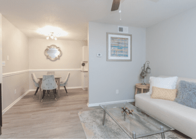 A living room with a creme-colored couch and glass top coffee table. The room is open to the dining area beyond