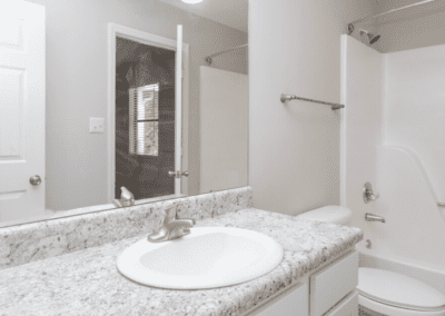 A white bathroom. in the mirror we can see two doors, though it is unclear where they lead.