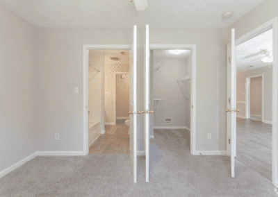 An empty bedroom with light carpet, a walk-in closet, and an en-suite bathroom