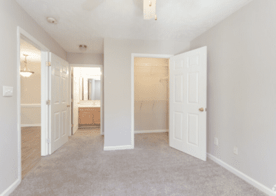 An empty bedroom with light carpet, a walk-in closet, and an en-suite bathroom