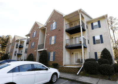 A large, three-story apartment building with white and brick siding in the Woodland Ridge apartment community. Each unit has either a balcony or a porch area