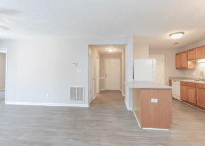 An open living room, dining room, and galley kitchen with wood cabinets and white appliances