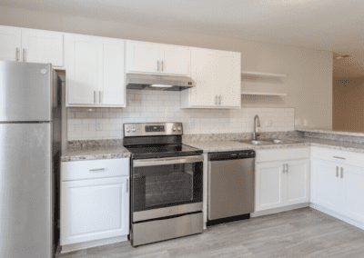 A large, open white kitchen with grey speckled countertops and stainless steel appliances