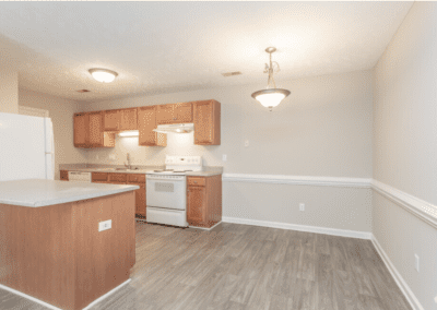 A galley-style kitchen with wood cabinets and white appliances with room for a dining area on the right