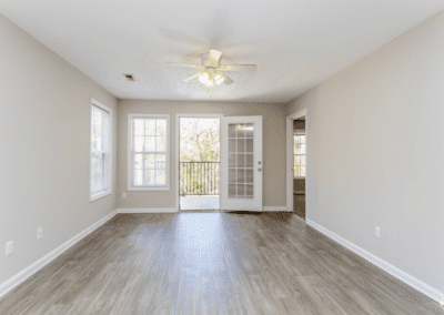 An empty living room with cool wood floors and a door that opens to the balcony