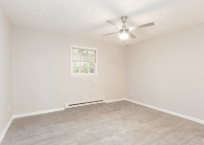 An empty room with light wood floors and a ceiling fan