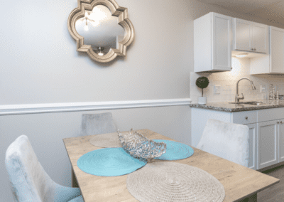 The dining room that is open to the kitchen. There is a wooden dining table and white suede chairs.