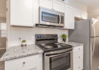 One side of a kitchen with white cabinets, a white tile backsplash, and stainless steel appliances