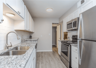 A galley-style kitchen with white cabinets, marbled white granite countertops, and stainless steel appliances.